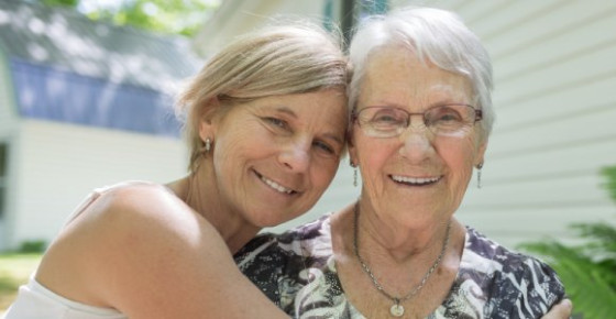 A younger woman rests her head against a more senior woman. Both are smiling